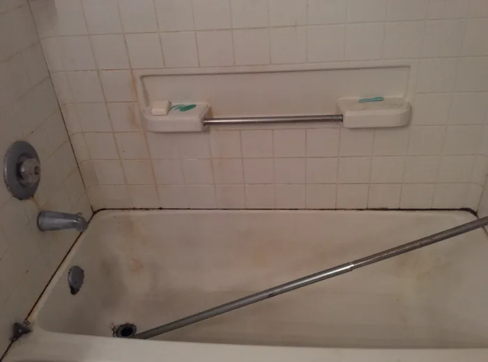 A stained bathtub and tiled surround before cleaning
